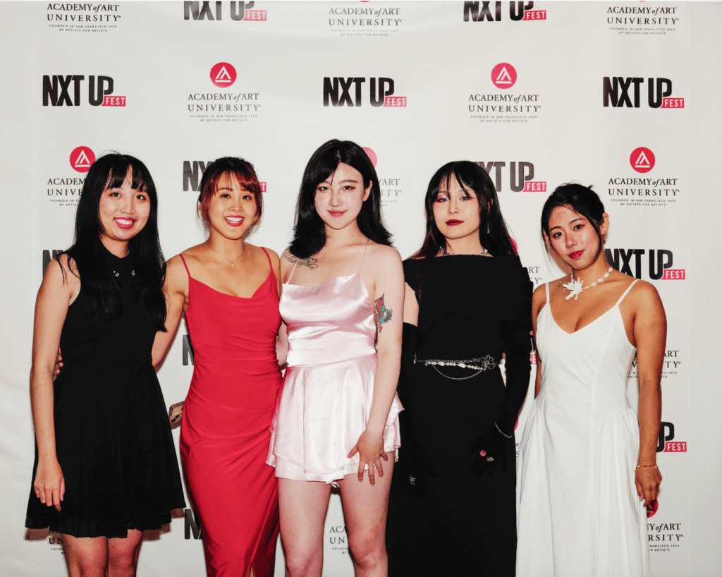Five people pose in fashionable attire against a backdrop featuring "NXT UP FEST" and "Academy of Art University" logos. Each wears a distinct outfit, showcasing diverse styles.